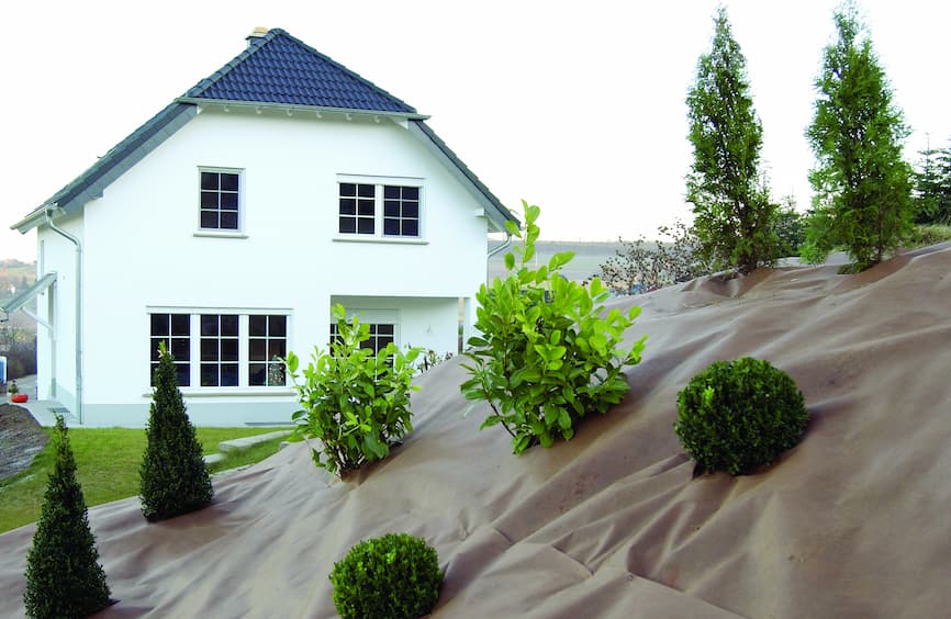 DuPont Plantex Gold folija protiv korova položena na padini pokraj kuće s izrezanim otvorima za biljke prije prekrivanja